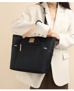 Detail view of a black nylon tote bag with leather handles shown on a white blazer model