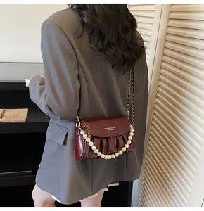 Détail d'un sac à plis bordeaux avec une poignée en perles et une bandoulière en métal