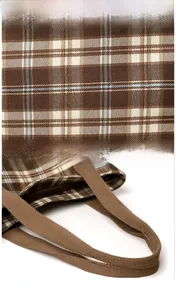 Detail of brown plaid tote showing textured fabric, woven handles and metal zipper