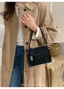 Close-up of black retro baguette bag with silver studs worn with a trench coat