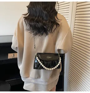 Détail du sac nuage plissé noir brillant avec chaîne en perles et logo doré élégant