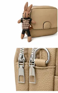 Detail of khaki leather mini round bag showing silver zippers and cute bunny pendant
