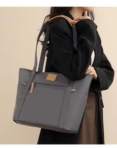 Detail view of large grey tote bag with front zipper pocket and brown leather logo tag