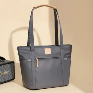Minimalist grey waterproof nylon tote bag with brown leather handles and side pockets