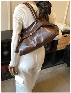 Detail of high-gloss dark brown patent leather tote bag with silver buckle worn by a model
