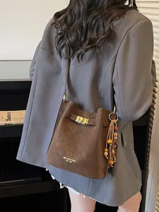 Braune Wildleder-Eimertasche mit Goldbeschlägen und Boho-Quaste an einem Modell