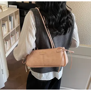 Detail of pink faux leather baguette bag with ribbon bow and fashion logo on model's shoulder