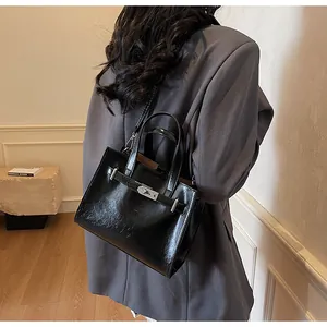 Détail d'un sac à main en cuir noir brillant avec fermoir argenté et anses arrondies