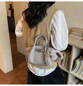 Detail of light grey pebbled leather bucket bag with metal lock and plush rabbit charm