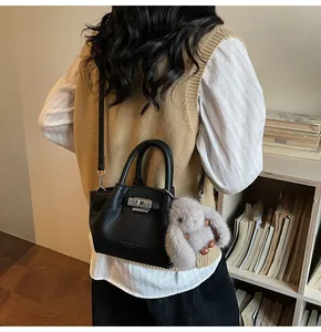 Close-up of black lychee grain leather bucket bag with silver lock and plush bunny charm
