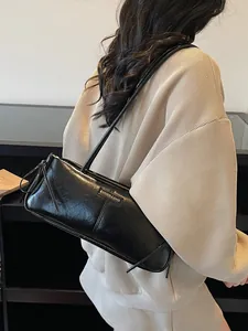 Glossy black Boston shoulder bag with dual straps worn by a model in a minimalist setting