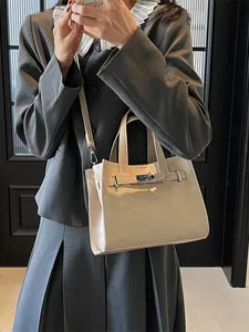 Sac à main beige minimaliste avec fermoir métallique porté par un mannequin en costume