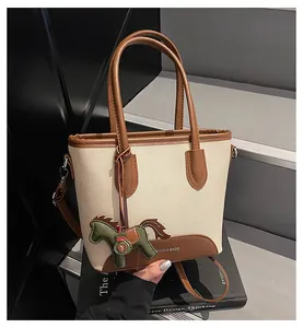 Detalle del bolso de lona con ribete de cuero y un amuleto decorativo de caballo verde