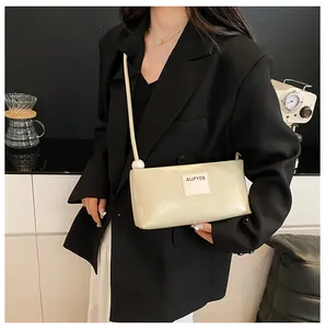 Détail du sac baguette crème avec une grande perle et logo sur cuir synthétique lisse