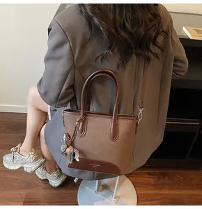 Vista detallada del bolso cubo marrón con ribete de cuero y un elegante colgante