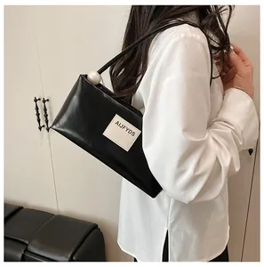 Détail du sac baguette noir en similicuir avec une grande perle et l'écusson de marque