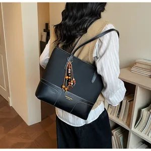 Détail du sac fourre-tout noir avec patchwork cuir-toile et pompon perlé sur la bandoulière
