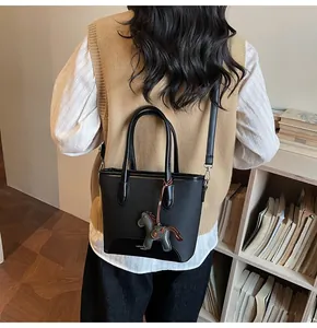 Detalle de un bolso cubo de cuero negro con colgante de caballo en una escena de biblioteca
