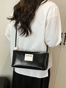 Sac baguette noir minimaliste en cuir brillant avec une grande perle sur la bandoulière