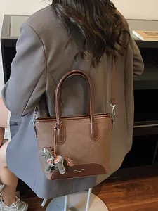 Bolso tipo cubo de lona y cuero marrón llevado cruzado por una modelo en chaqueta