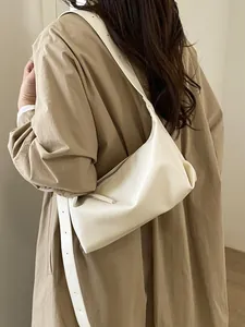 Minimalist beige leather baguette bag shown as a shoulder bag on a model
