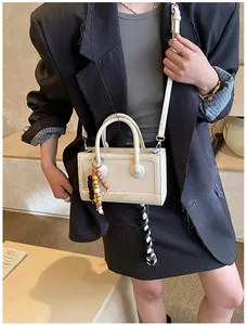 Détail du sac baguette minimaliste beige crème avec breloque perlée et bandoulière