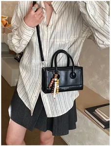 Détail du sac baguette noir avec pompon en perles de bois et bandoulière en cuir