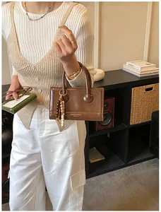 Détails du sac baguette en cuir marron avec chaîne perlée et logo de marque gravé