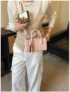 Détail d'un sac à main en cuir rose avec poignées et breloque en perles sur un modèle