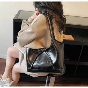 Détail du cabas noir brillant avec nœud décoratif et texte GONGZHU embossé sur le cuir