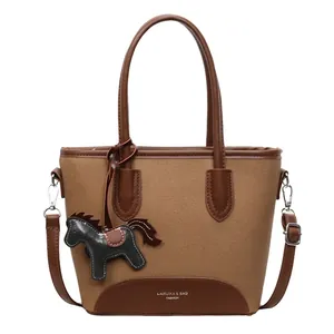 Bolso cubo minimalista de lona marrón con correas de cuero y colgante de caballo