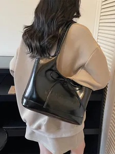 Sac fourre-tout noir élégant avec détail de ruban et finition polie porté à l'épaule