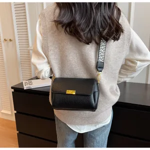 Détail du sac baguette en cuir noir avec boucle dorée et bandoulière tissée géométrique