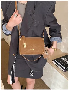Détail d'un sac carré en cuir mat marron avec fermoir métallique et breloque ours en peluche