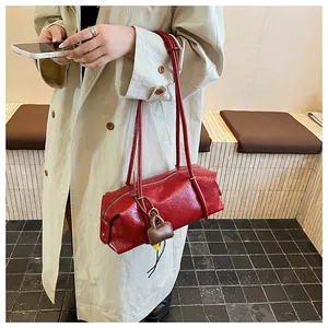 Detail view of red leather baguette bag with thin shoulder straps and mini charm on model