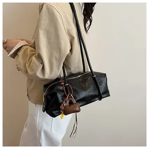 Detail of a black glossy wrinkled baguette bag with decorative charms on model's shoulder
