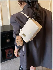 Détail d'un sac crème avec rivets dorés, fermoir rotatif et breloque en peluche