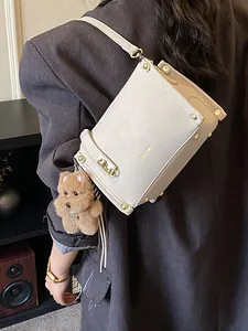 Sac bandoulière beige chic avec détails dorés et breloque peluche sur veste sombre