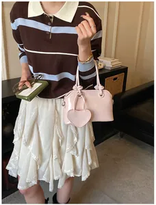 Detail of light pink patent leather shell bag with knotted handle and heart pendant