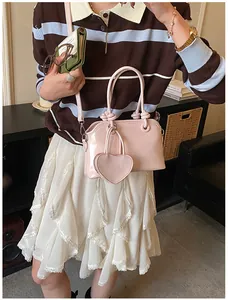 Close-up of light pink glossy patent leather shell bag with brand logo and heart pendant