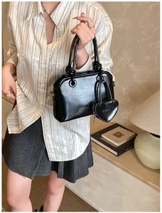 Close-up of glossy shell handbag with heart-shaped charm and Brooda embossed logo