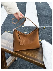 Detail of a brown suede shoulder bag with adjustable strap on a park bench