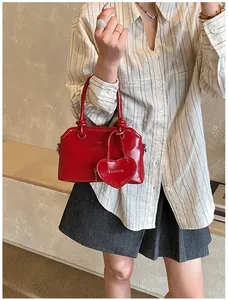Detail of red glossy shell handbag with heart charm shown on model in minimal room