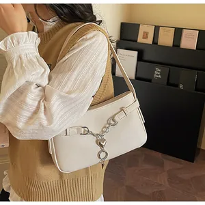 Detail of cream white faux leather underarm bag with silver chain and heart charm decoration