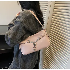 Close-up of a pink leather baguette bag with silver heart chain charms on a female model