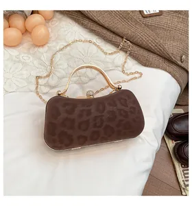 Détail de la pochette léopard avec poignée dorée et fermoir à strass sur tissu blanc