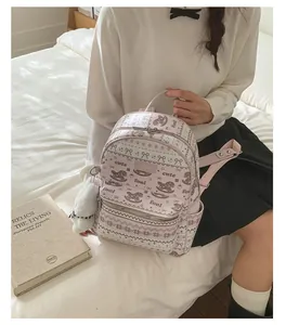 Detail of pink floral backpack with bow prints and white plush ball charm accessory