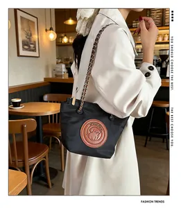 Détail du sac bandoulière en nylon noir avec écusson en cuir et bandoulière chaîne