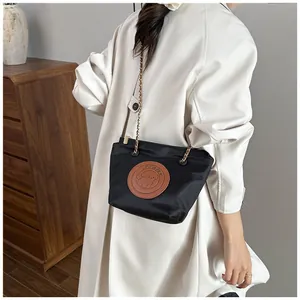 Détail d'un cabas en nylon noir avec écusson en cuir et chaîne dorée porté par un mannequin