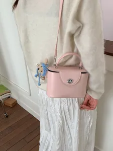 Pink matte leather square handbag with crochet cat charm shown on model's shoulder